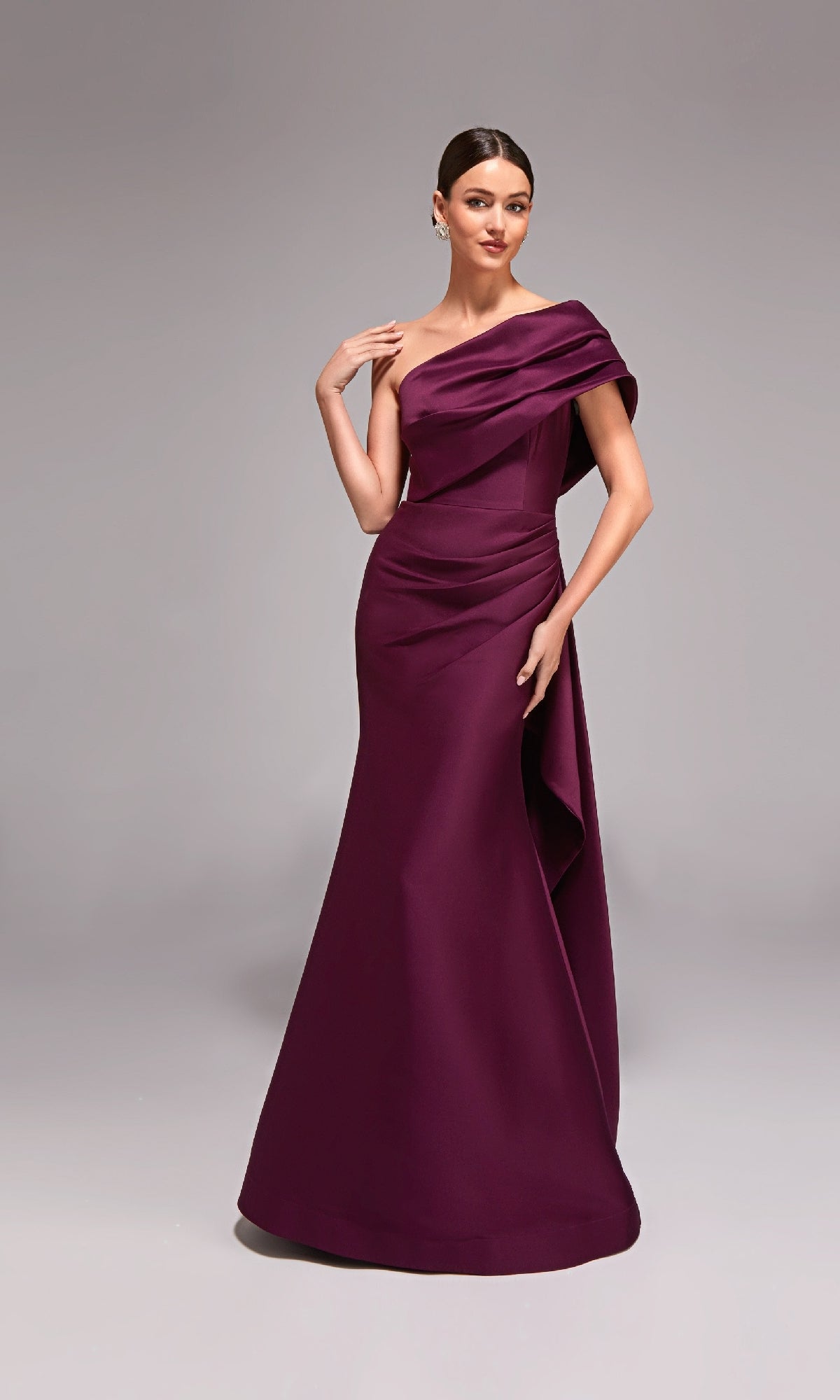 A woman models the Alyce 27838 long formal dress in elegant, off-shoulder eggplant, posing against a plain gray background.